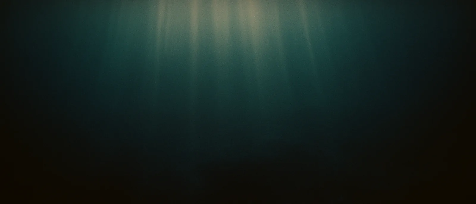 Underwater view of fading light columns descending into deep blue-black ocean, layered shadow, no visible seafloor